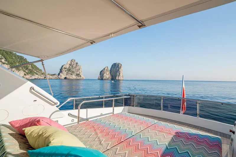 Gemini 3 Yacht Photos Pics Luxurious Maiora 24S yacht deck with colorful cushions, overlooking serene ocean and rock formations.