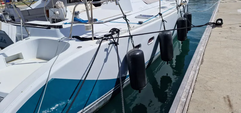 Lambada Yacht Photos Pics Lagoon 47 catamaran from 1993 docked with fenders, reflecting on calm water.
