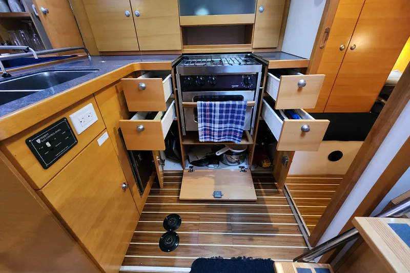 Danza Yacht Photos Pics 2007 Hanse 400e yacht kitchen with open cabinets and stove, featuring wooden cabinetry.