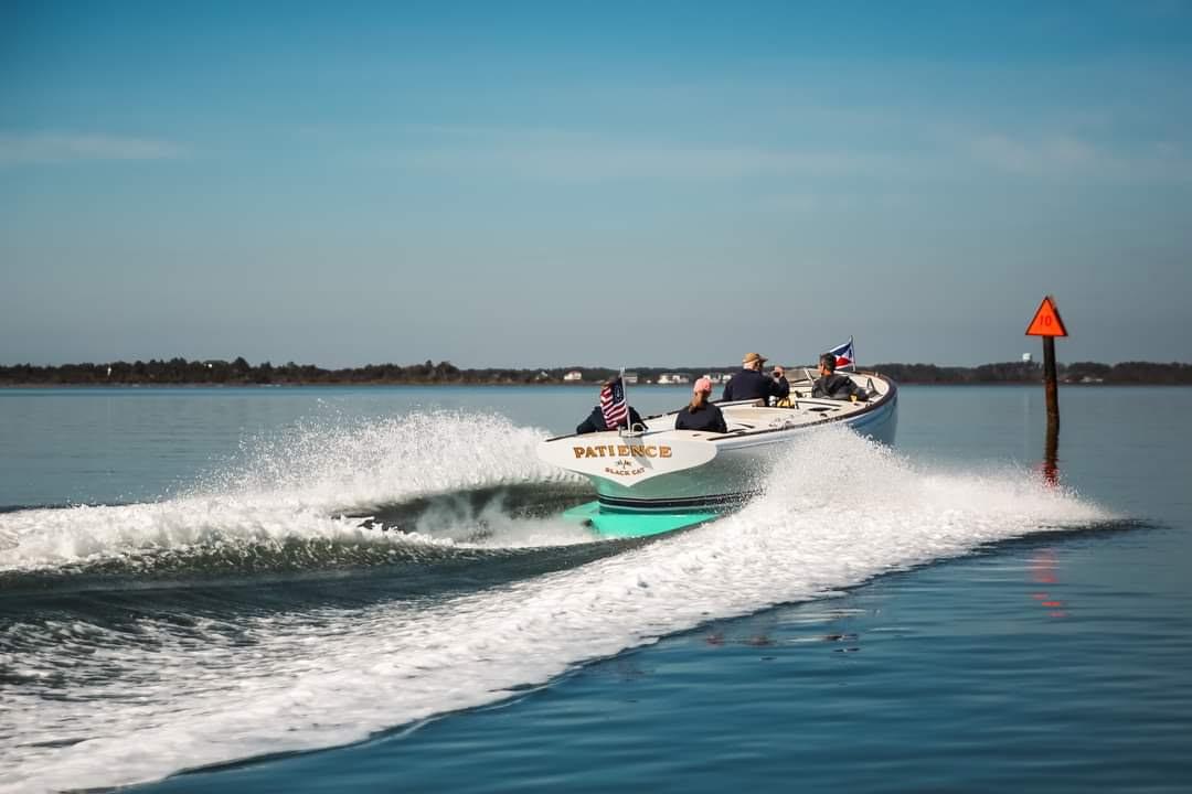 Custom M27 boat cruising on calm water, 2023 model, with flags and wake trail.