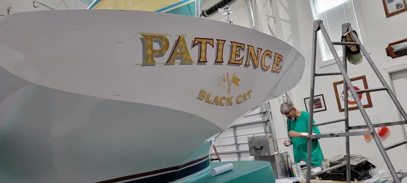 Patience Yacht Photos Pics Custom M27 boat named "Patience" in a workshop, with a person working nearby.