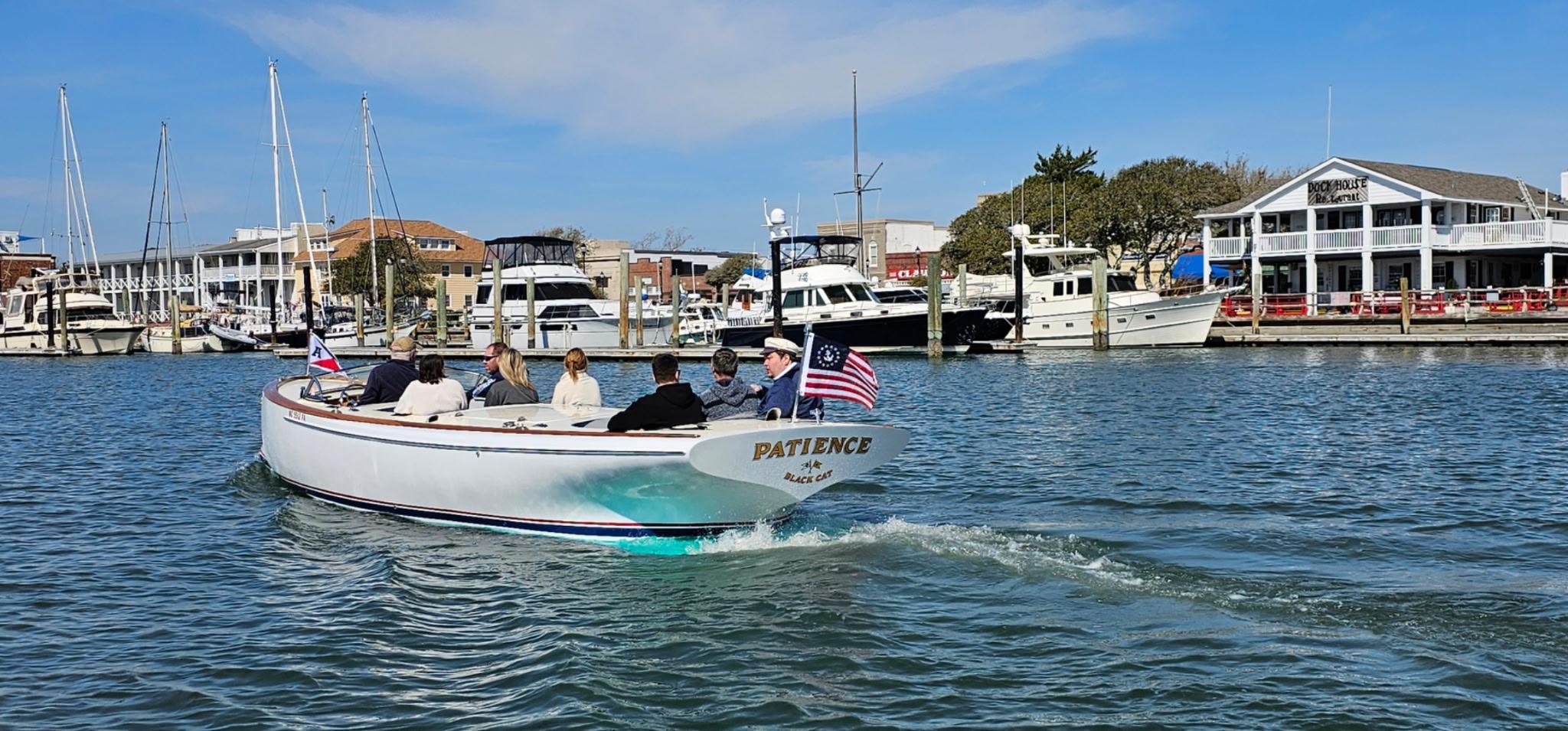 A custom 2023 M27 boat named "Patience" cruising in a marina with passengers.