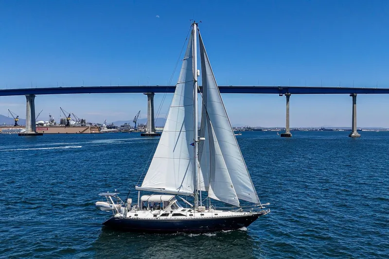 Dea Latis Yacht Photos Pics Sailboat Hylas 49 (2001) cruising under a large bridge on a sunny day.