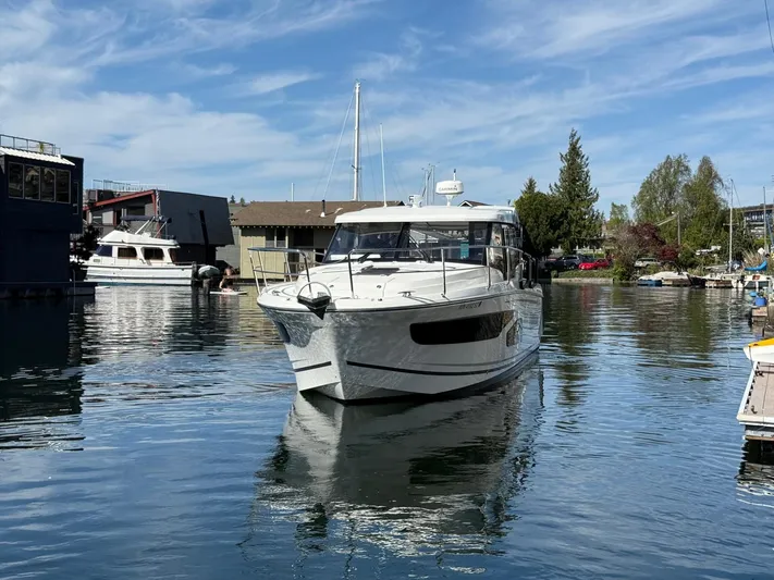  Yacht Photos Pics 2021 Jeanneau NC Weekender 1095 boat on calm water, surrounded by marina and trees.