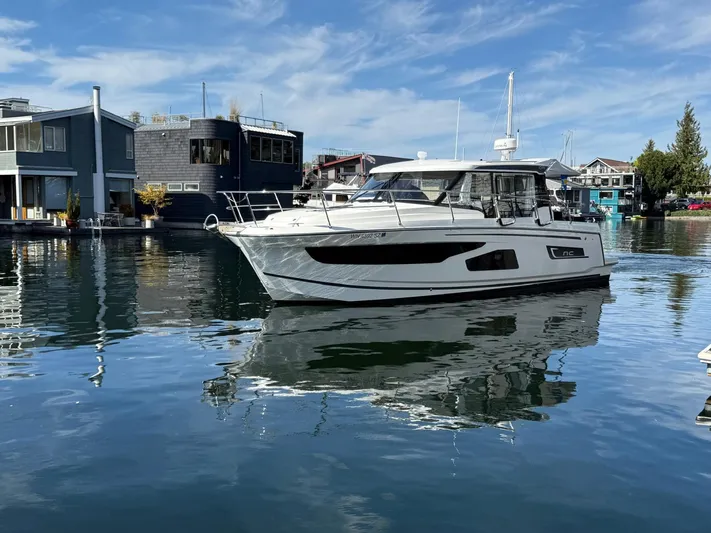  Yacht Photos Pics 2021 Jeanneau NC Weekender 1095 boat docked on calm water, modern waterfront homes in background.