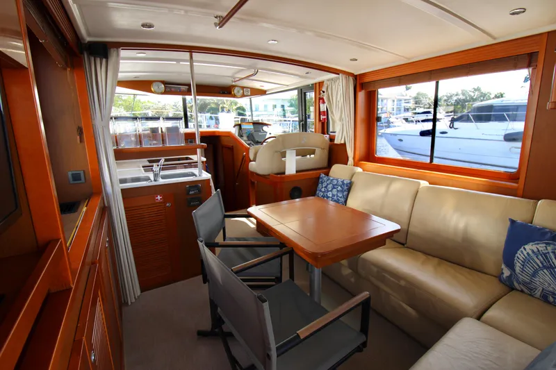 Next Chapter Yacht Photos Pics Interior of 2014 Beneteau Swift Trawler 44 with beige seating, wooden table, and large windows.