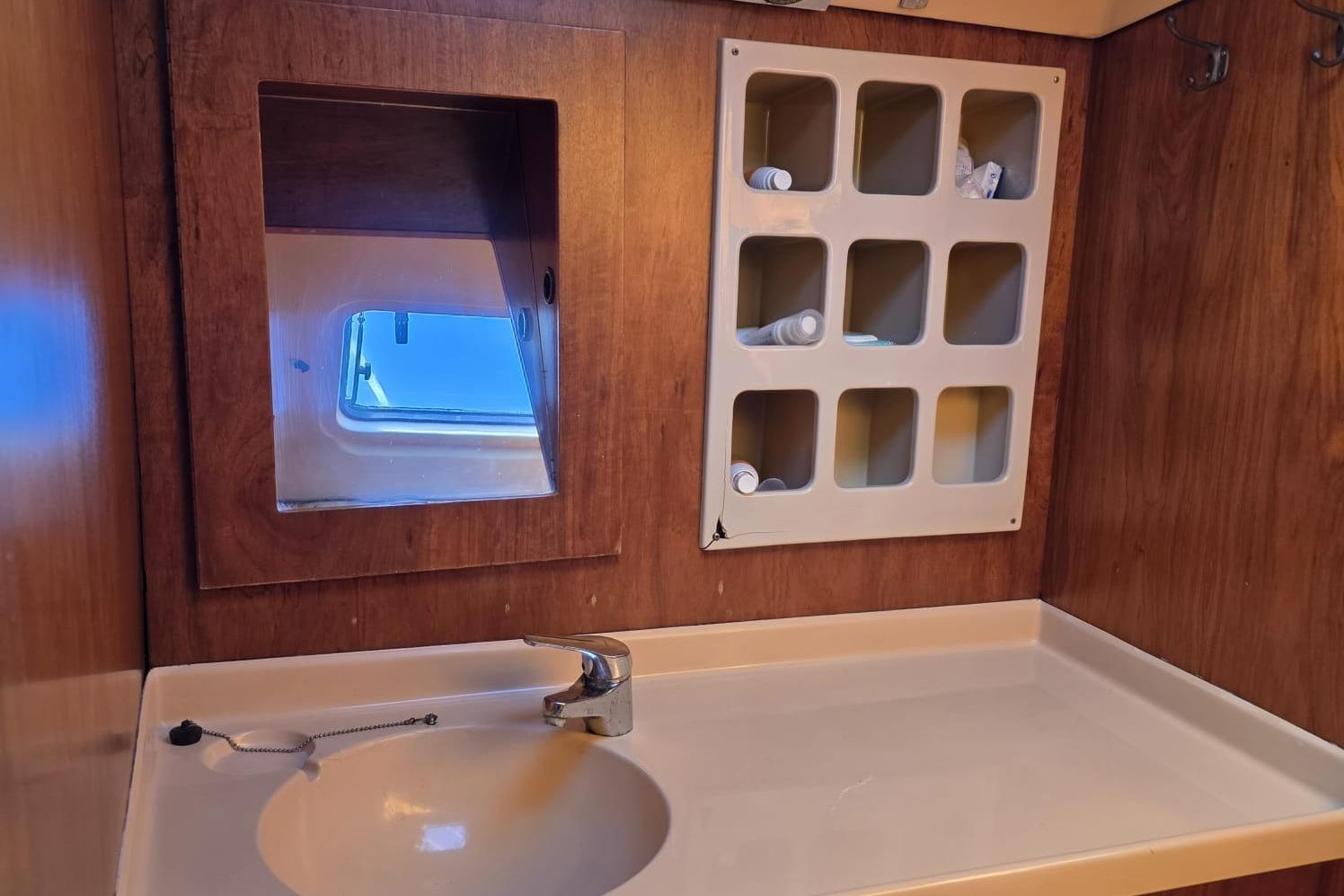 1981 Comar Comet 11 yacht bathroom with sink, mirror, and storage compartments.