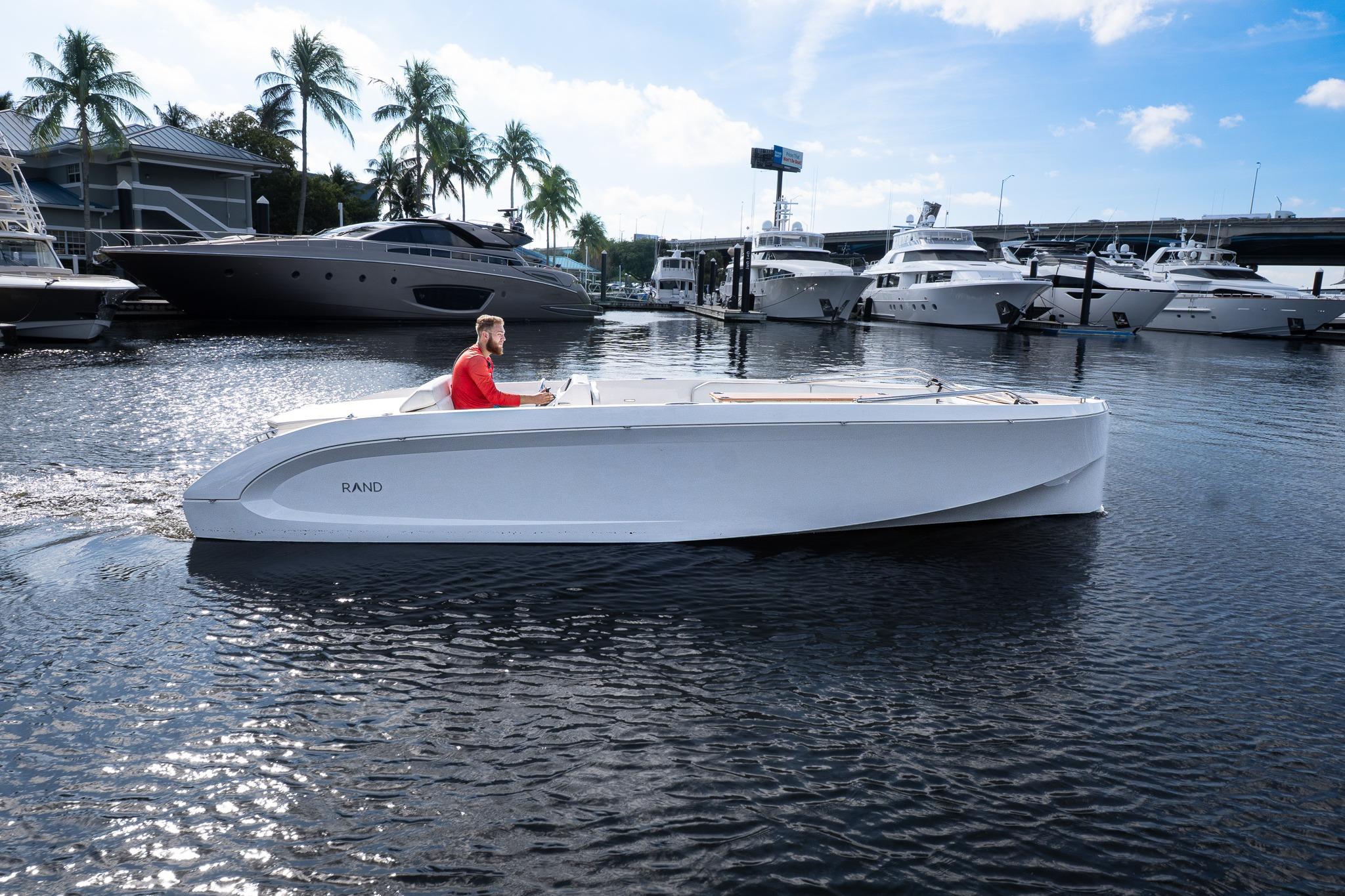 2022 Rand 23 Mana boat cruising in marina with yachts and palm trees in background.