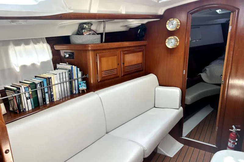 Dionysus Yacht Photos Pics Interior of 2003 Beneteau Oceanis Clipper 473 with books, white seating, and wooden cabinetry.