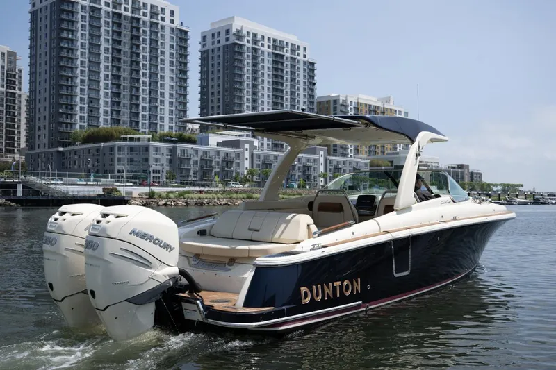 Dunton Yacht Photos Pics 2021 Chris-Craft Launch GT boat cruising near modern waterfront buildings.