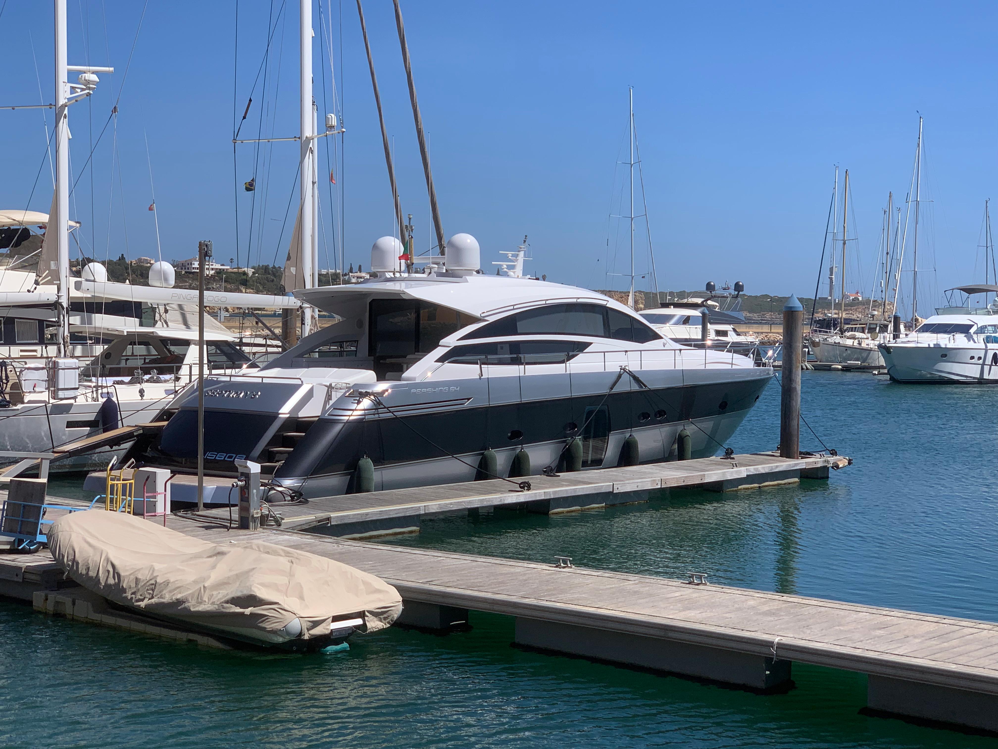 Luxury Pershing 64 yacht docked in marina, 2010 model, clear blue sky.