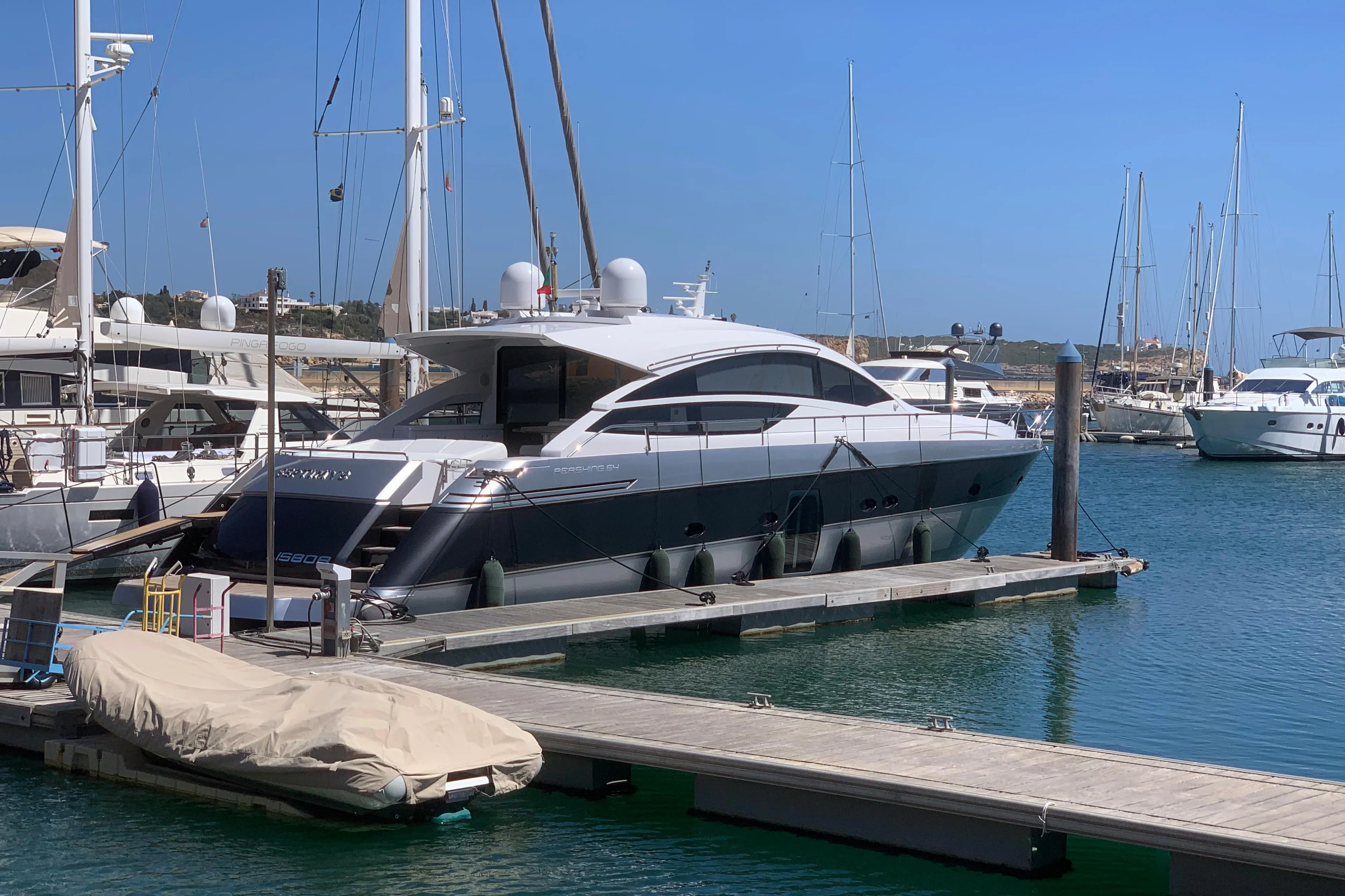 Luxury Pershing 64 yacht docked in marina, 2010 model, clear blue sky.
