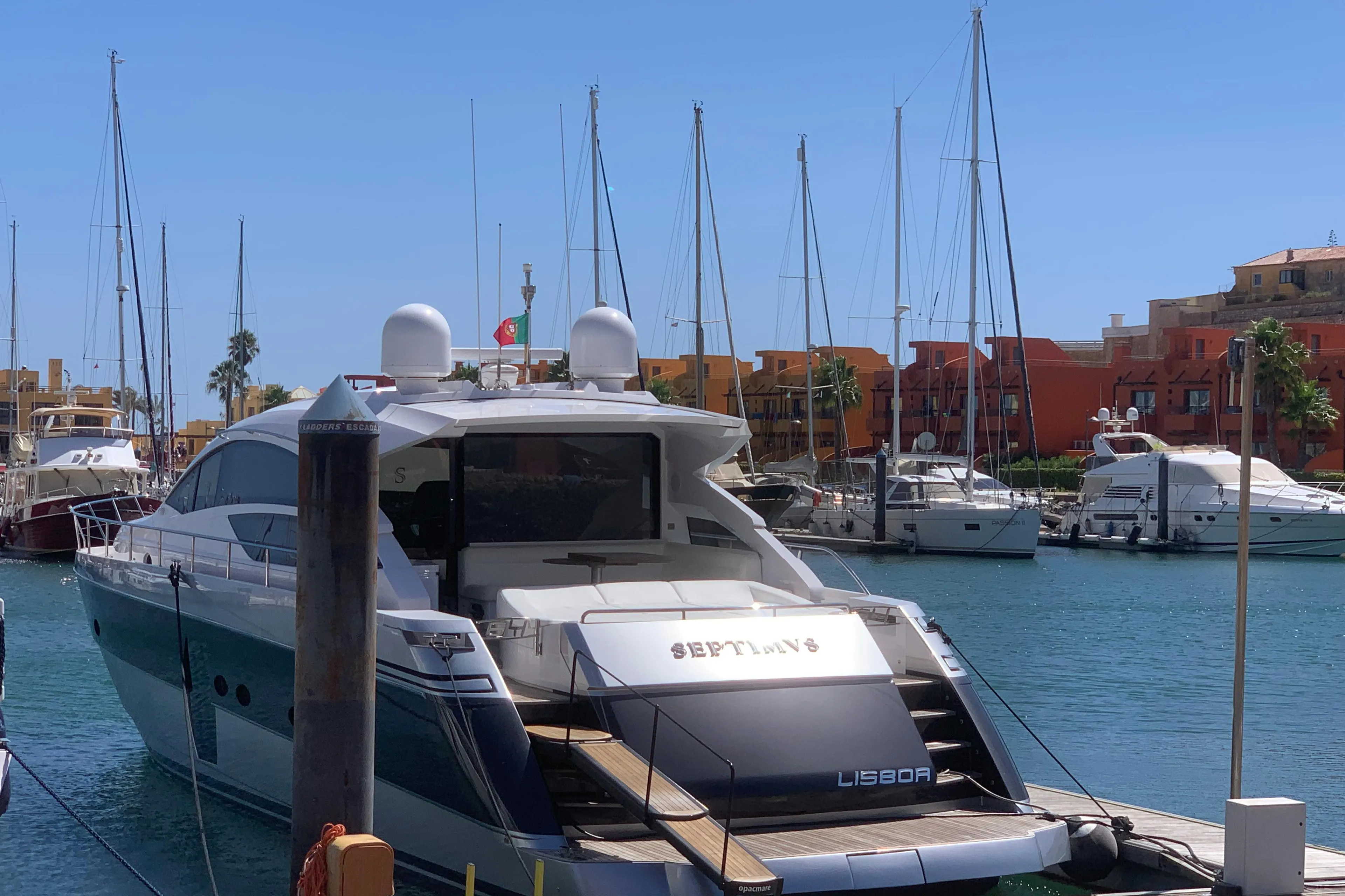 Luxury Pershing 64 yacht docked in marina, 2010 model, with sailboats and colorful buildings in background.