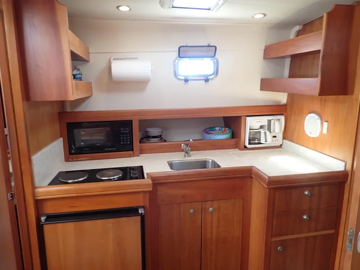  Yacht Photos Pics 2004 Mainship 34 Rum Runner II galley with stove, sink, microwave, and wooden cabinetry.