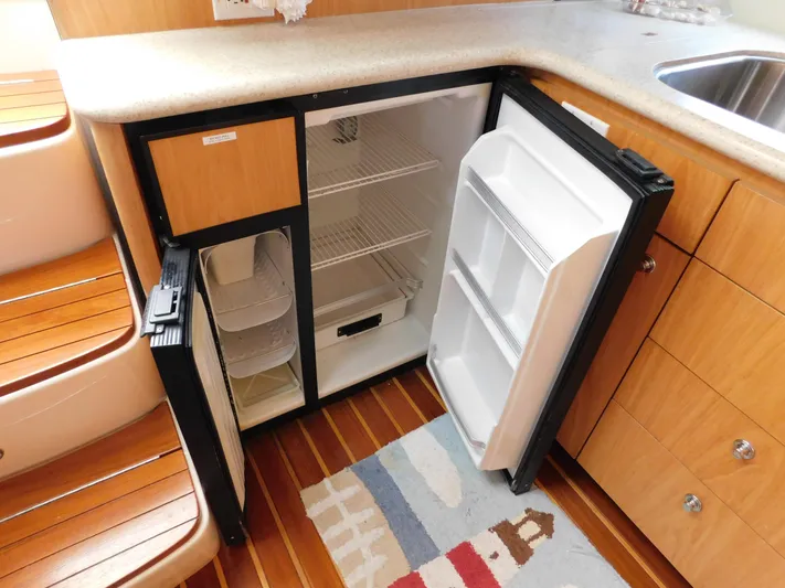 Cap & Dan Yacht Photos Pics Open mini fridge in 2001 Tiara Yachts 3800 Open, wooden interior, compact kitchen space.
