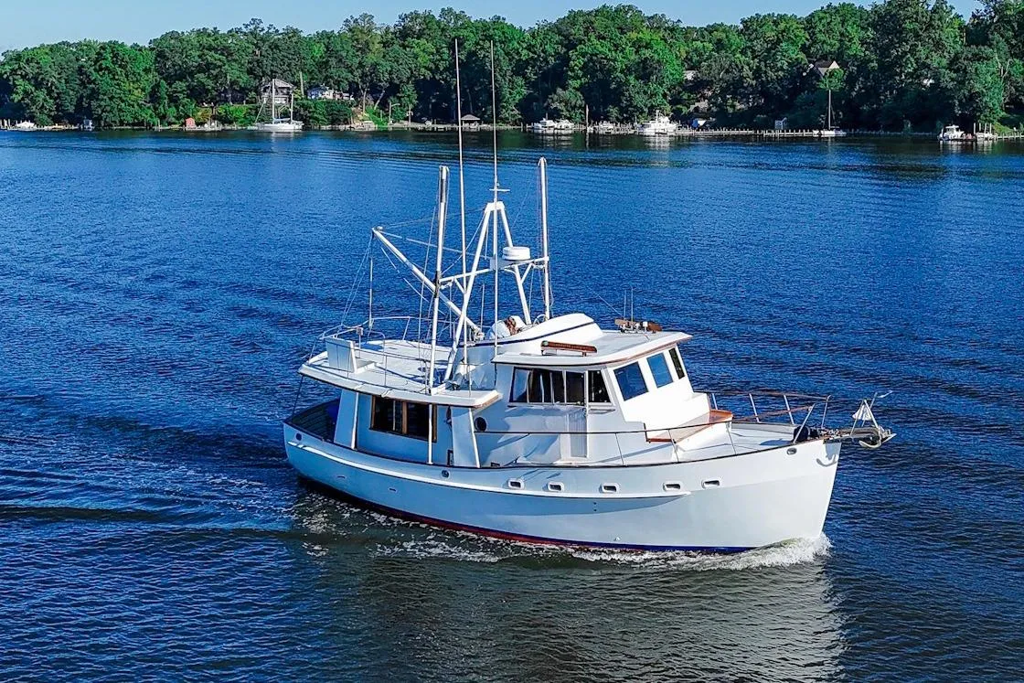 1983 Kadey-Krogen Krogen 42 Trawler cruising on a serene lake with lush green shoreline.