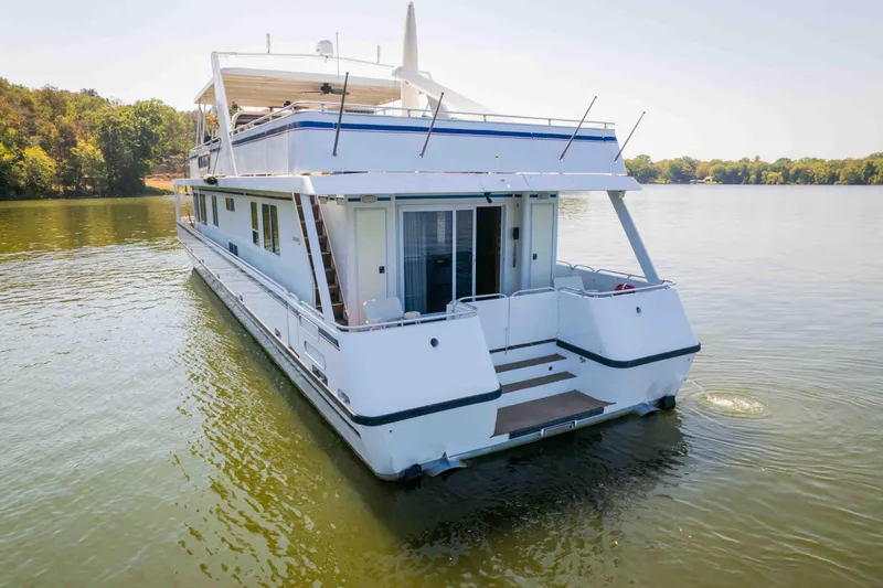  Yacht Photos Pics 2004 Stardust Cruisers houseboat on a serene lake, surrounded by lush greenery.