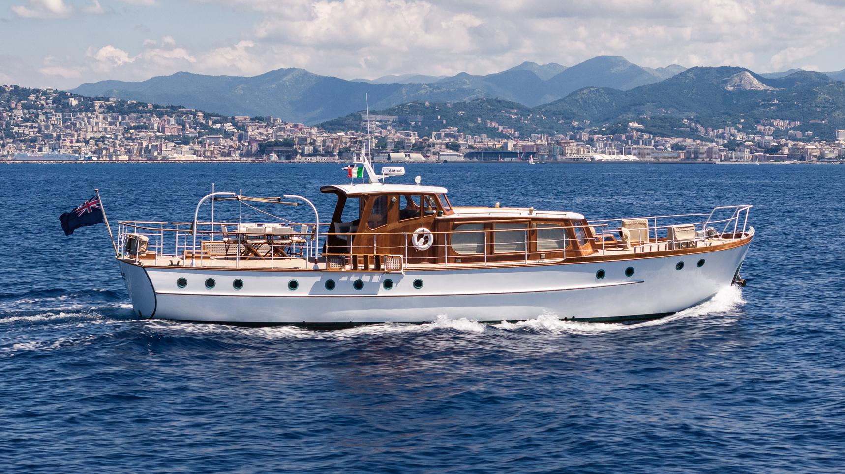 Vintage 1961 Silver James A yacht cruising on blue waters with scenic coastal backdrop.