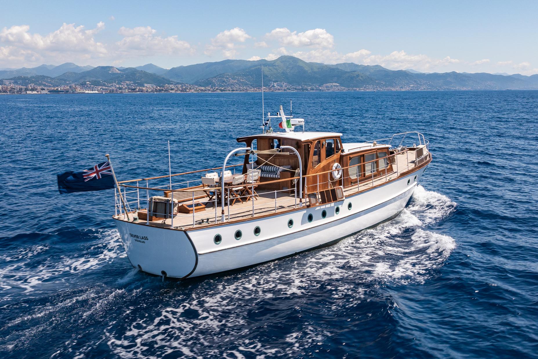1961 James A Silver yacht cruising on blue ocean waters with scenic mountain backdrop.