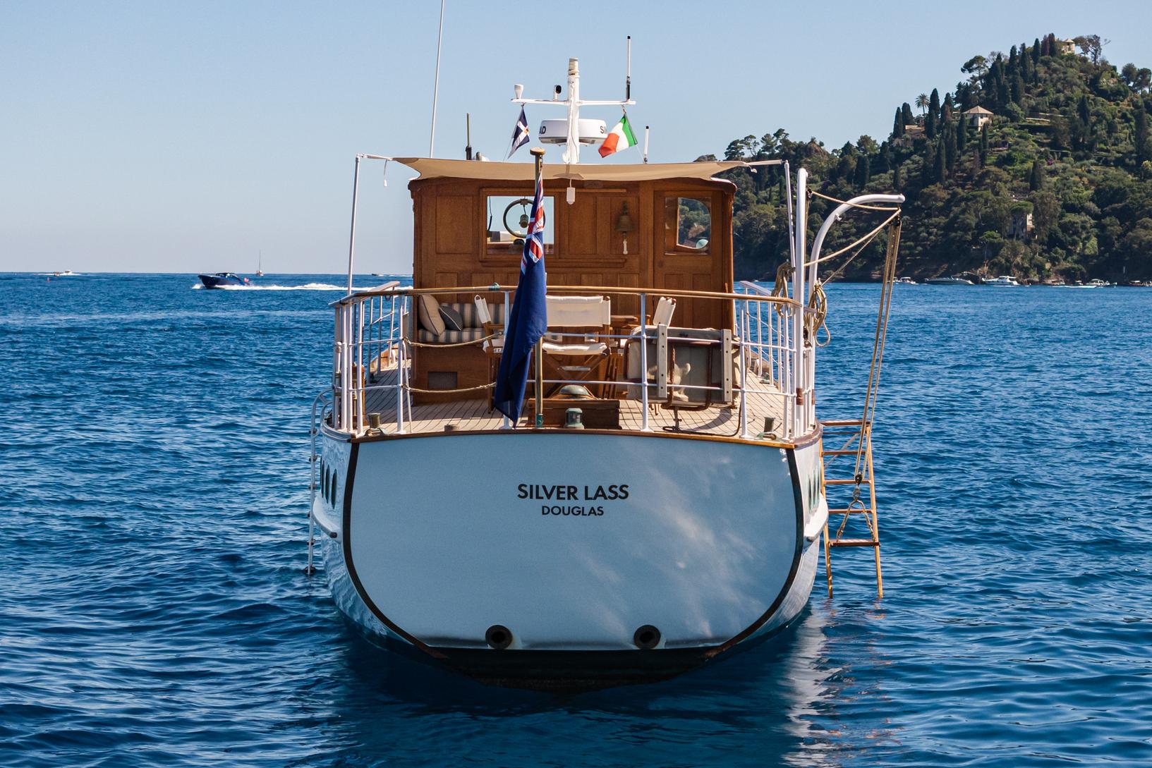 1961 Silver James A Silver boat 'Silver Lass' on blue ocean near forested coastline.