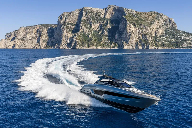  Yacht Photos Pics 2025 Riva Capri 58 yacht cruising near rocky coastline under clear blue sky.