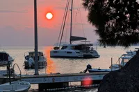 Sunset over marina with 2018 Leopard 45 catamaran, tranquil sea, and silhouetted trees.