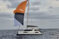 2018 Leopard 45 catamaran sailing with vibrant orange and gray spinnaker on open sea.