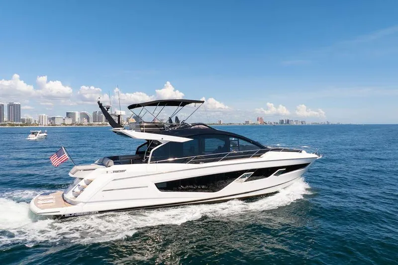  Yacht Photos Pics 2023 Sunseeker 65 Sport Yacht cruising on open water, city skyline in background.
