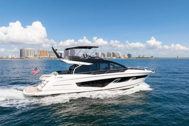  Yacht Photos Pics 2023 Sunseeker 65 Sport Yacht cruising on open water, city skyline in background.