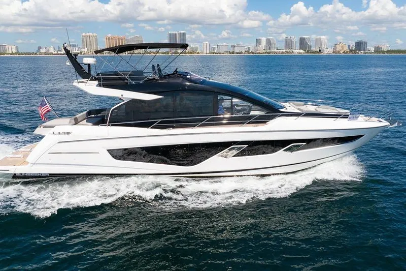  Yacht Photos Pics 2023 Sunseeker 65 Sport Yacht cruising on open water with city skyline backdrop.