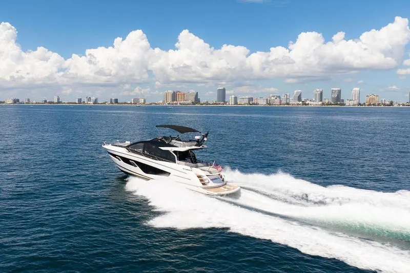  Yacht Photos Pics 2023 Sunseeker 65 Sport Yacht cruising on open water with city skyline backdrop.