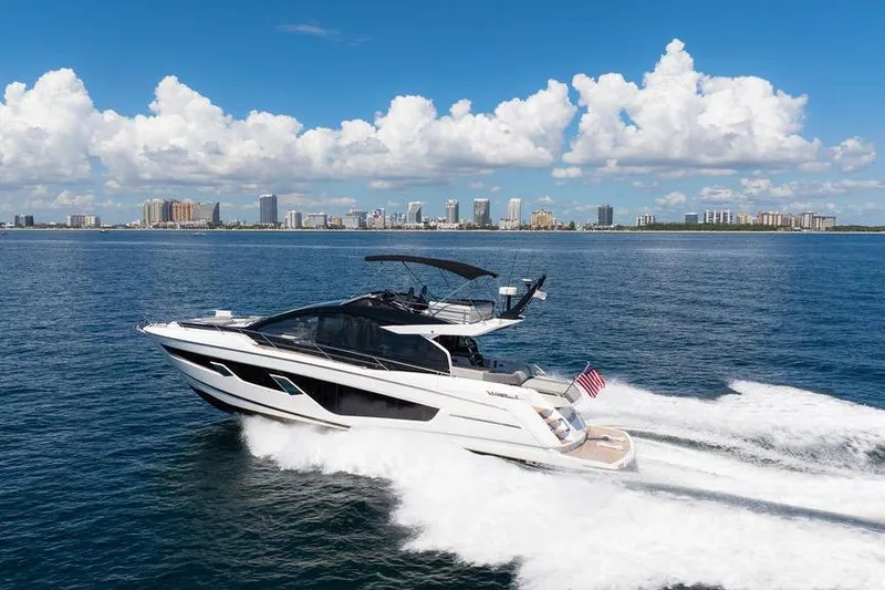  Yacht Photos Pics 2023 Sunseeker 65 Sport Yacht cruising on open water with city skyline backdrop.