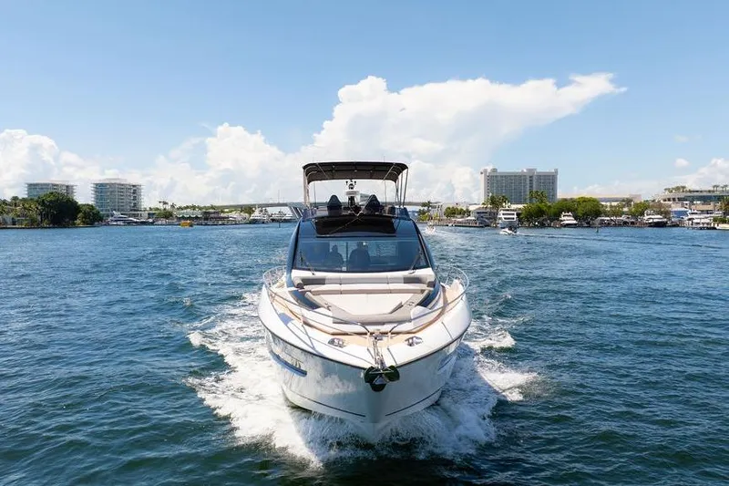  Yacht Photos Pics 2023 Sunseeker 65 Sport Yacht cruising on a sunny day, with cityscape in the background.