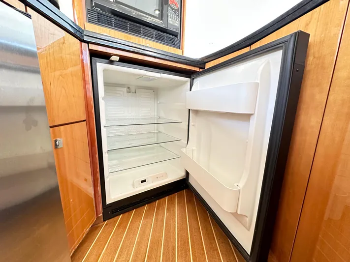 Lai Lani Yacht Photos Pics Empty refrigerator inside 2005 Sunseeker Manhattan 66 yacht, featuring wooden cabinetry and striped flooring.