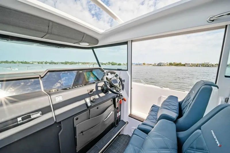  Yacht Photos Pics 2022 Axopar 37 Cross Cabin interior with steering wheel and blue seats, overlooking water.