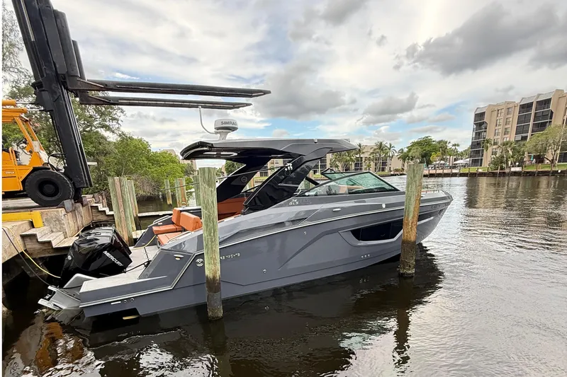 Kailani II Yacht Photos Pics 2023 Cruisers Yachts 34 GLS OB docked on a calm river with modern buildings.