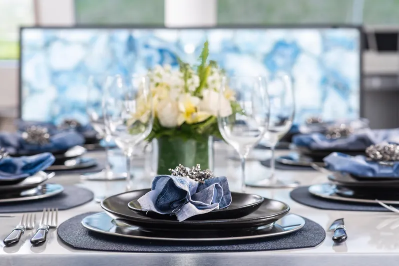 Relentless II Yacht Photos Pics Elegant dining setup on 2022 Sunreef 80 Sail yacht, featuring blue accents and floral centerpiece.