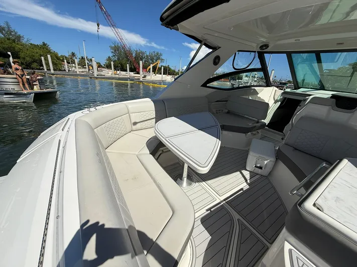  Yacht Photos Pics 2022 Sea Ray Sundancer 320 Outboard interior with seating and table, docked near water.