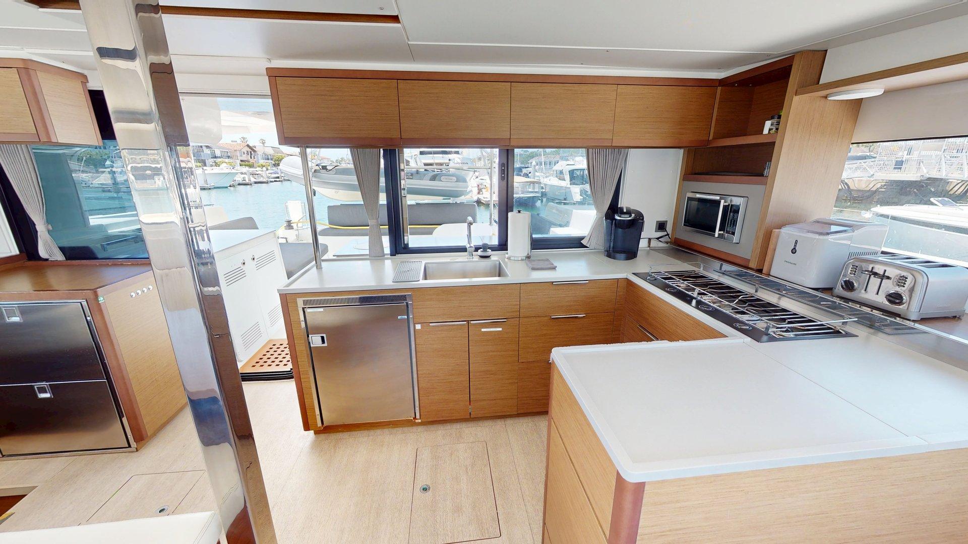 Modern kitchen interior of 2020 Lagoon 46 yacht with appliances and wooden cabinetry.
