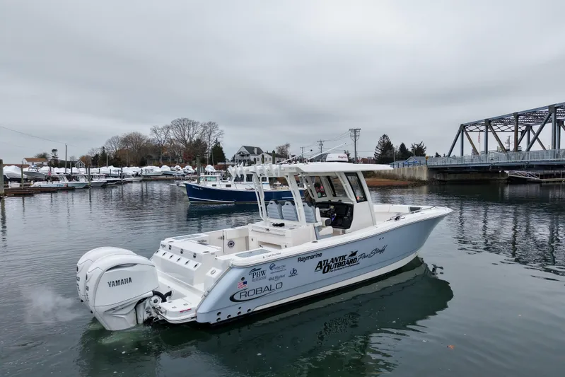  Yacht Photos Pics 2025 Robalo R300 Center Console boat on calm water near a bridge.
