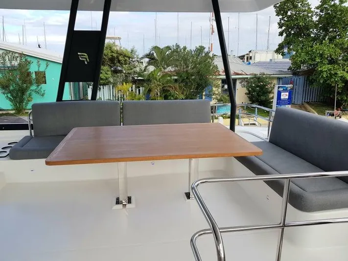 Calypso Yacht Photos Pics 2021 Fountaine Pajot MY6 yacht deck with seating and table, surrounded by greenery.