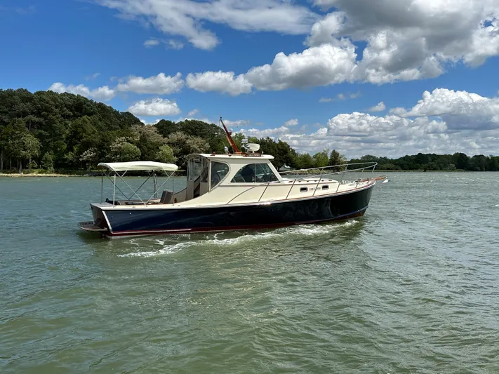  Yacht Photos Pics 2001 Mast & Mallet 38 Picnic Boat cruising on a scenic lake under a partly cloudy sky.