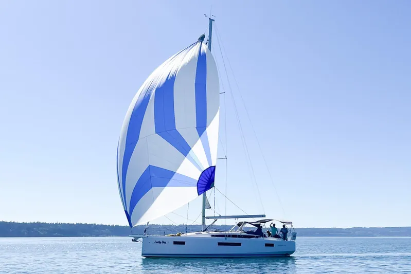 Lucky Dog Yacht Photos Pics 2023 Jeanneau Sun Odyssey 410 sailing with blue and white spinnaker on calm waters.