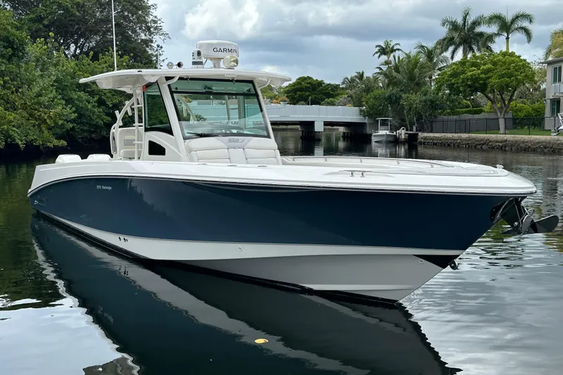  Yacht Photos Pics 2015 Boston Whaler 370 Outrage boat on calm water, surrounded by lush greenery.