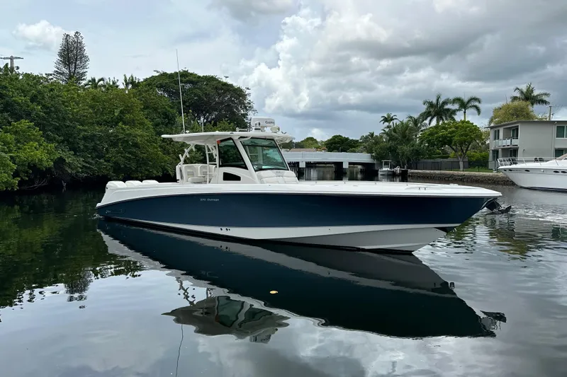  Yacht Photos Pics 2015 Boston Whaler 370 Outrage boat on calm water, surrounded by lush greenery.
