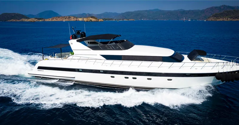  Yacht Photos Pics Luxurious 1999 Mangusta 105 yacht cruising on open sea with scenic mountain backdrop.