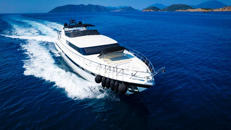  Yacht Photos Pics Luxurious 1999 Mangusta 105 yacht cruising on open sea with scenic island backdrop.
