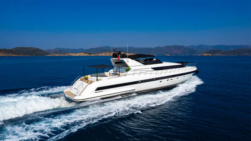  Yacht Photos Pics Luxurious 1999 Mangusta 105 yacht cruising on open sea with scenic mountain backdrop.