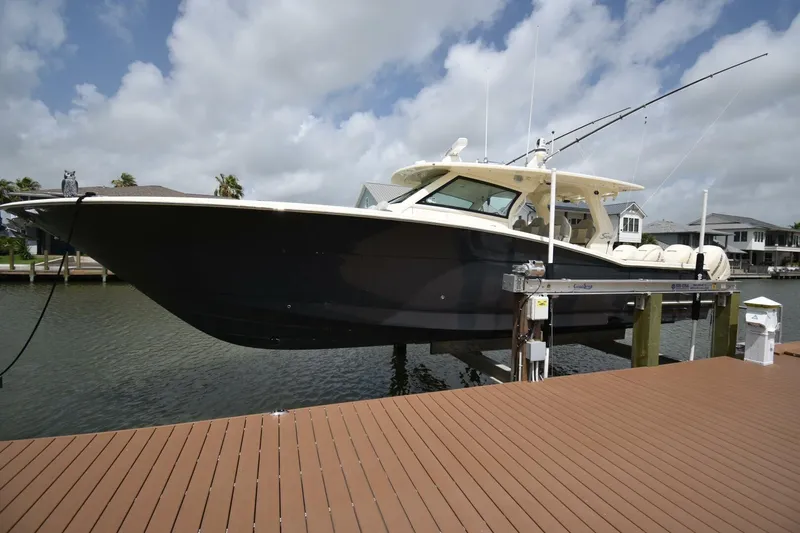  Yacht Photos Pics 2022 Scout 425 LXF boat docked on a lift, with fishing rods, under a cloudy sky.