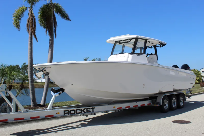  Yacht Photos Pics 2024 Fountain 32 NX boat on trailer, parked near palm trees and water.